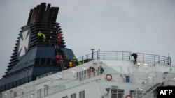 Firemen attempt to get migrants to come down from a ferry funnel on March 3, 2019 in French port of Calais, after migrants hoping to reach Britain scrambled aboard a cross-Channel ferry, sparking a vast police sweep of the ship.