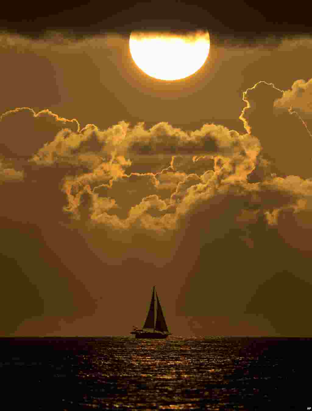 A sailboat is silhouetted by the rising sun, as it passes by the coast of Surfside, Florida.