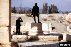 A Syrian army soldier takes a picture of a fellow soldier standing on ruins in the historic city of Palmyra, Syria, March 4, 2017.