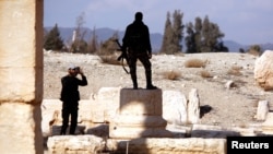 A Syrian army soldier takes a picture of a fellow soldier standing on ruins in the historic city of Palmyra, Syria, March 4, 2017.