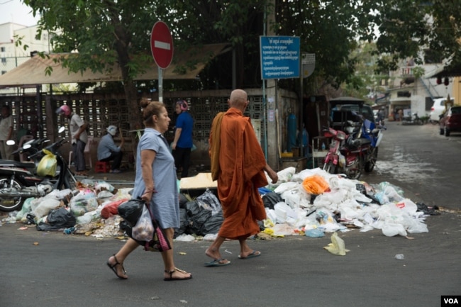 រូបឯកសារ៖ ស្រ្តី​ម្នាក់​និង​ព្រះសង្ឃ​មួយ​អង្គ​ ដើរកាត់​គំនរ​សម្រាម​ នៅ​ក្នុង​រាជធានី​ភ្នំពេញ កាលពី​ថ្ងៃទី​២៦ ខែធ្នូ ឆ្នាំ២០១៨។ (ទុំ ម្លិះ/VOA)