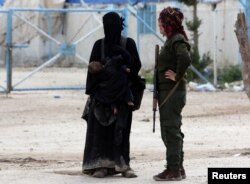 A fighter of the Syrian Democratic Forces (SDF) stands next to the wife of an Islamic State militant in al-Hol displacement camp in Syria, April 1, 2019.