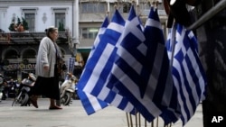 A woman walk past Greek flags for sale in central Athens, Greece as it runs perilously short of cash amid an impasse in bailout talks with its international creditors, April 22, 2015.