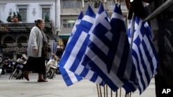 FILE - A woman walk past Greek flags for sale in central Athens, Greece as it runs perilously short of cash amid an impasse in bailout talks with its international creditors, April 22, 2015.