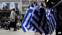 FILE - A woman walks past Greek flags for sale in central Athens, April 22, 2015.