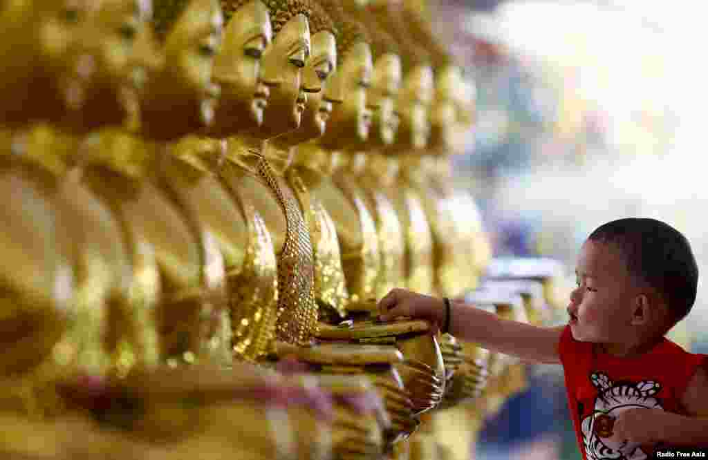 Seorang anak meletakkan koin ke patung emas Buddha, sebagai simbol keberkahan pada Hari Raya Waisak di Candi Chetawan, Petaling Jaya, Malaysia.