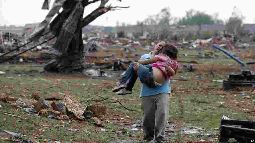 A woman carries her child through a field near the collapsed Plaza Towers Elementary School in Moore, Oklahoma, May 20, 2013.