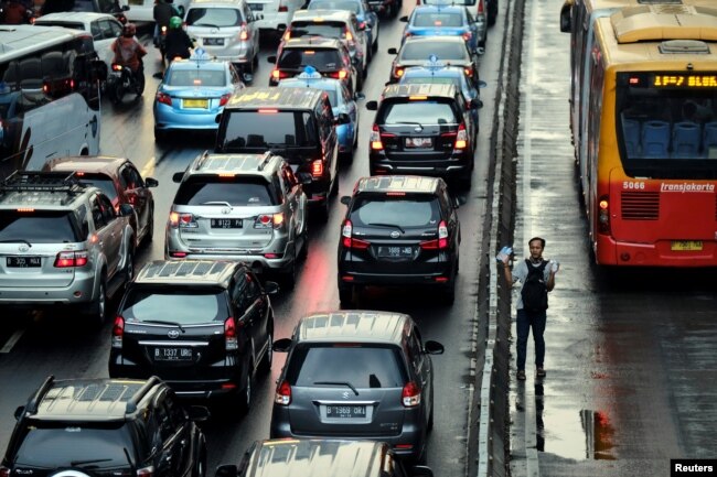 Seorang penjaja minuman menawarkan air minum kepada pengendara mobil dan motor yang terjebak macet di jalan Sudirman Jakarta, 13 Juni 2017.