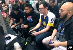 In this Aug. 25, 2017, photo, Connor Nguyen, at right, and Griffin Williams, second from right, compete in a "Super Smash Bros. Melee" tournament at the Shine eSports festival at the Seaport World Trade Center in Boston, Massachusetts. (AP Photo/Collin Binkley)