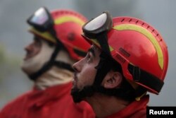 Firefighters take a break to watch planes dump water on a forest fire in Mendeira, Portugal, June 19, 2017.