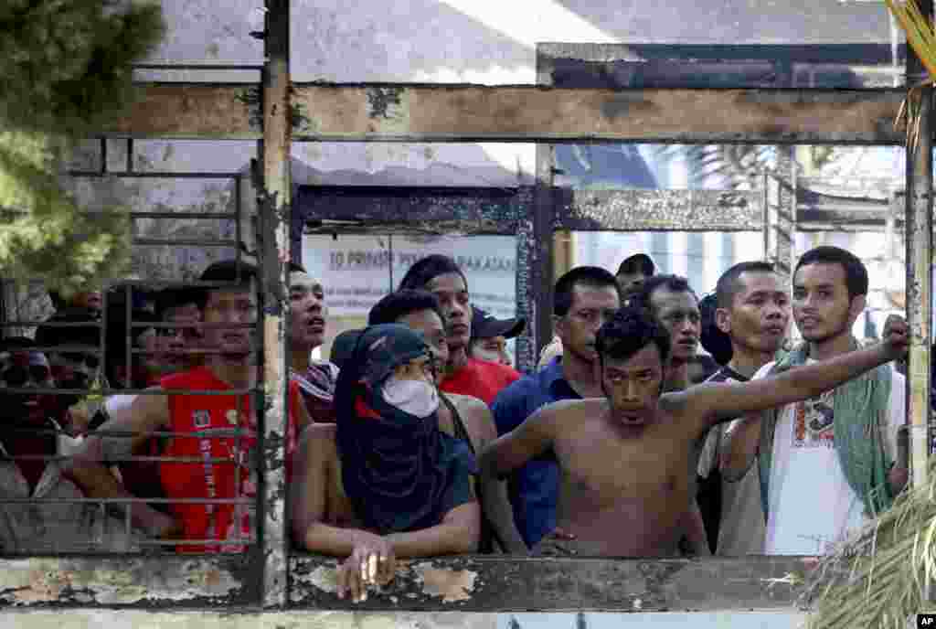 Para penghuni LP Tanjung Gusta mengintip dari balik kantor yang terbakar (12/7) menyusul kerusuhan di penjara itu sehari sebelumnya. (AP/Binsar Bakkara)