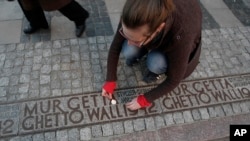 FILE - A woman lights a candle in a place where a border wall stood during World War II separating the Warsaw ghetto from the rest of the town, in Warsaw, Poland, April 21, 2013. 