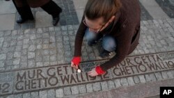 FILE - A woman lights a candle in a place where a border wall stood during World War II separating the Warsaw ghetto from the rest of the town, in Warsaw, Poland, April 21, 2013.