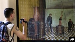 A tourist takes a photo of a painting depicting how Tuol Sleng prisoners were tortured by Khmer Rouge soldiers. 