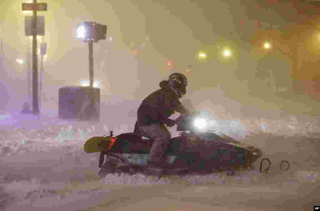 A man uses a snowmobile to travel along a street before dawn during a winter snowstorm in Boston, Massachusetts, Jan. 27, 2015.