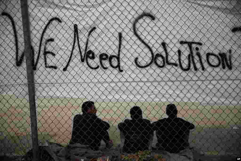 Migrants sit below a banner outside a former Olympic indoor stadium in Faliro, southern Athens, Greece.