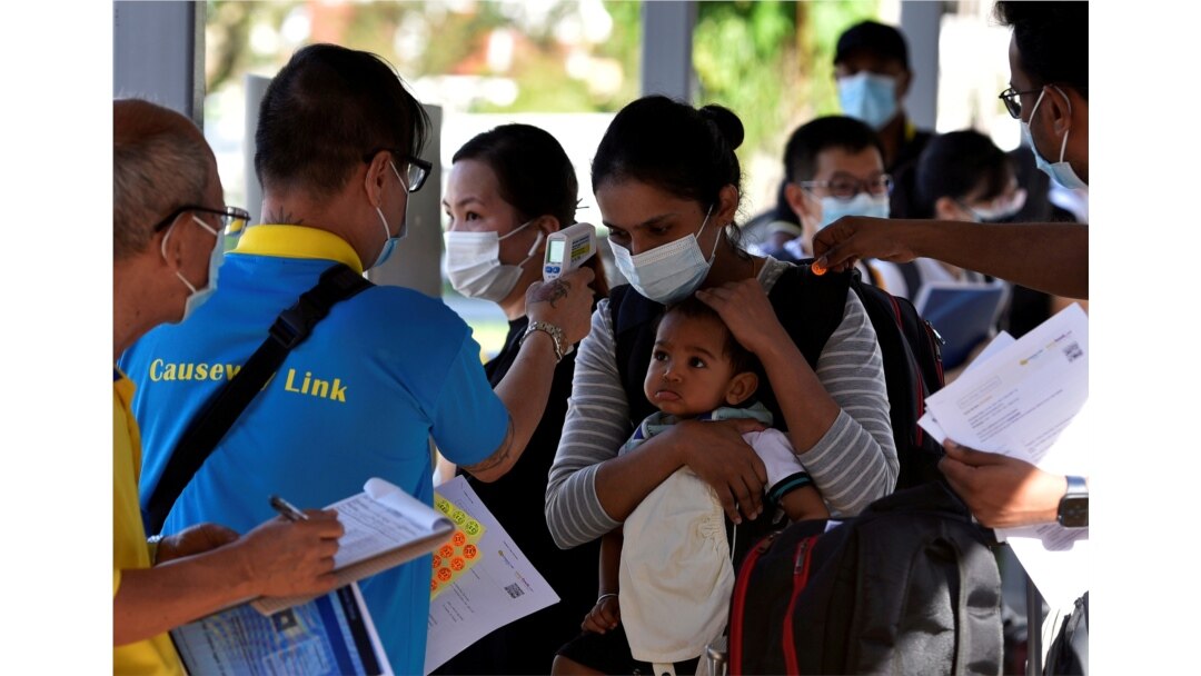 Seorang ibu dan anak diperiksa suhu tubuhnya saat bersiap untuk naik bus kembali ke Malaysia, di sebuah terminal bus di Singapura, 29 November 2021. (Foto: REUTERS/Caroline Chia)