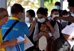 Seorang ibu dan anak diperiksa suhu tubuhnya saat bersiap untuk naik bus kembali ke Malaysia, di sebuah terminal bus di Singapura, 29 November 2021. (Foto: REUTERS/Caroline Chia)