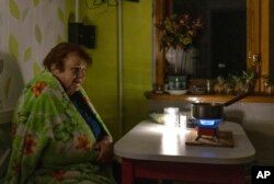 An elderly woman cooks food on a gas burner during a blackout in Kyiv, Ukraine, Nov. 14, 2022.