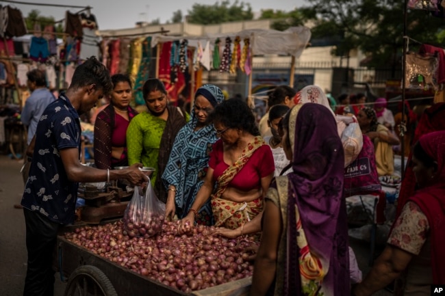 A roadside vendor packs onions in plastic bags as women shop at a weekly market in New Delhi, India, Wednesday on June 29, 2022. (AP Photo/Altaf Qadri)