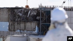 FILE - A media person wearing a protective suit and a mask looks at the No. 3 reactor building at Tokyo Electric Power Co's (TEPCO) tsunami-damaged Fukushima Dai-ichi nuclear power plant in Okuma, Fukushima Prefecture, Japan, Feb. 10, 2016. 