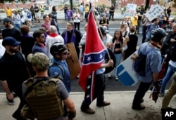 FILE - A white supremacists carries the Confederate flag as he walks past counter demonstrators in Charlottesville, Va., Aug. 12, 2017.