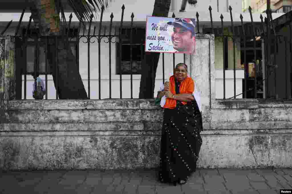 A cricket fan poses for photographers while holding a placard of cricketer Sachin Tendulkar outside a stadium in Mumbai, Nov. 14, 2013. 