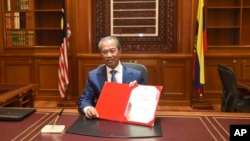 In this photo released by Malaysia's Department of Information, the country's new Prime Minister Muhyiddin Yassin poses for pictures on his first day at the prime minister's office in Putrajaya, Malaysia, Monday, March 2, 2020. (Hafiz Itam/Malaysia)