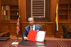 In this photo released by Malaysia's Department of Information, the country's new Prime Minister Muhyiddin Yassin poses for pictures on his first day at the prime minister's office in Putrajaya, Malaysia, Monday, March 2, 2020.