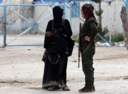 FILE - A fighter of the Syrian Democratic Forces (SDF) stands next to the wife of an Islamic State militant in al-Hol displacement camp in Syria, April 1, 2019.