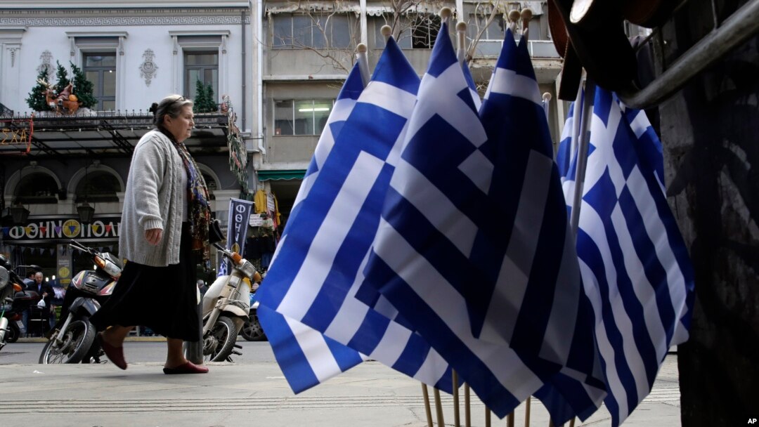 A woman walk past Greek flags for sale in central Athens, Greece as it runs perilously short of cash amid an impasse in bailout talks with its international creditors, April 22, 2015.