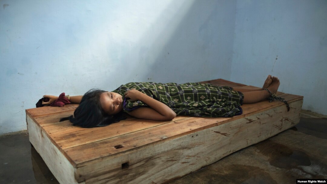 Perempuan berusia 24 tahun berbaring di bale-bale dengan pergelangan tangan dan kaki yang dirantai di pusat penyembuhan Bina Lestari di Brebes, Jawa Tengah. (Human Rights Watch/Andrea Star Reese)