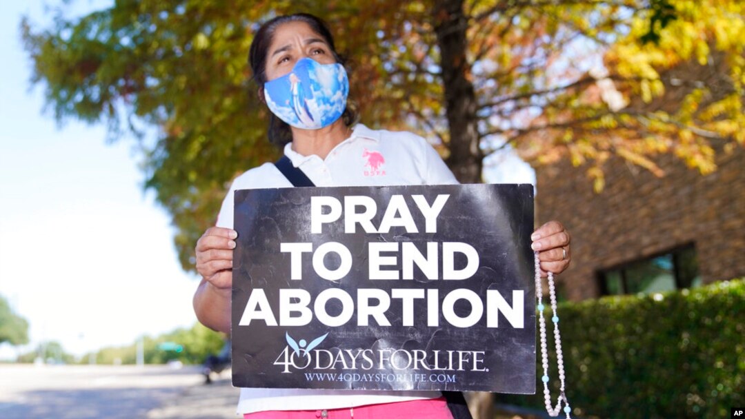 Maria Peña holds a rosary and sign out outside a building housing an abortion provider in Dallas, Oct. 7, 2021. 