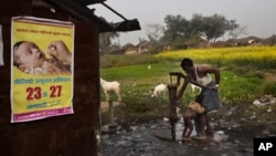 FILE - A man bathes a child with a water pump beside a polio awareness campaign poster on the wall of a small shop in the village of Kosi, some 180 kilometers (113 miles) from Patna, India. 