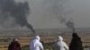 People look on as smoke rises from the Syrian town of Ras al-Ayn, in a picture taken from the Turkish side of the border in Ceylanpinar, Oct. 11, 2019, on the third day of Turkey's military operation against Kurdish forces. 