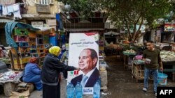 People walk past a campaign poster of Egypt's President Abdel Fattah al-Sisi in a market in Cairo on December 7, 2023, ahead of the nation's election.