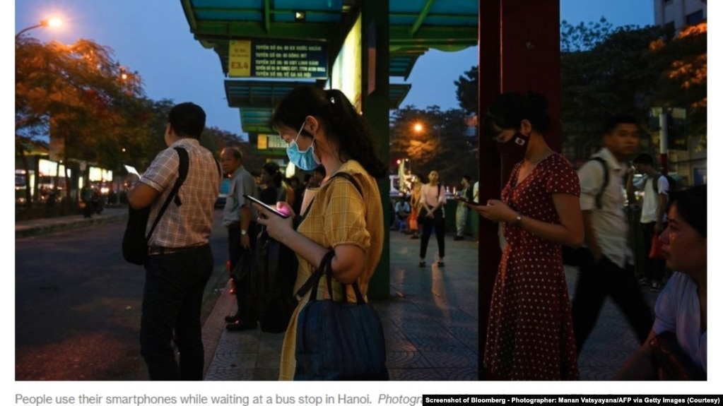 Nhiều người dùng điện thoại di động khi đứng chờ xe buýt ở Hà Nội. (Ảnh chụp màn hình Bloomberg - Photographer: Manan Vatsyayana/AFP via Getty Images)