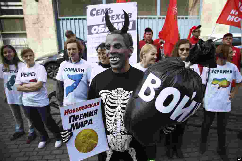 A Russian Communist Party activist, wearing a mask depicting US President Barack Obama, holds a poster reading "Nobel Peace Prize" in one hand and a bag reading "War" in the other, takes part at a picket outside the UN mission in Moscow, Russia, Sept. 9, 
