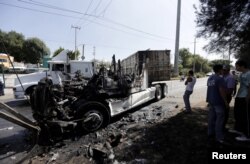 FILE - Men stand next to the wreckage of a tractor-trailer set ablaze by members of a drug cartel in Guadalajara, Mexico, May 1, 2015.