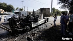 Men stand next to the wreckage of a tractor-trailer set ablaze by members of a drug cartel in Guadalajara, Mexico, May 1, 2015. 