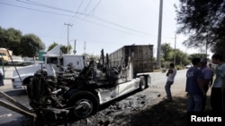 FILE - Men stand next to the wreckage of a tractor-trailer set ablaze by members of a drug cartel in Guadalajara, Mexico, May 1, 2015. 