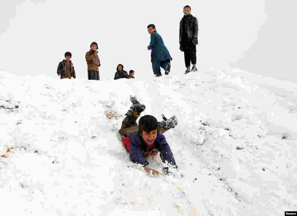 Boys slide down a snow-covered slope on the outskirts of Kabul, Afghanistan.