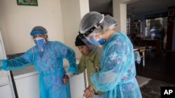 Nurses wearing protective gear walk with an elderly woman at the Mas Vida home for senior citizens in Lima, Peru, May 12, 2020. 