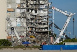 Workers peer up at the rubble pile at the partially collapsed Champlain Towers South condo building, ahead of a visit to the site by President Joe Biden, in Surfside, Florida, July 1, 2021.