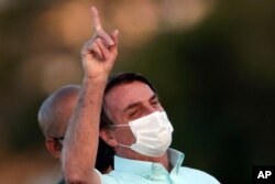 FILE - Brazil's President Jair Bolsonaro, who is infected with COVID-19, wears a protective face mask as he attends a Brazilian flag retreat ceremony outside his official residence the Alvorada Palace, in Brasilia, Brazil, July 22, 2020.