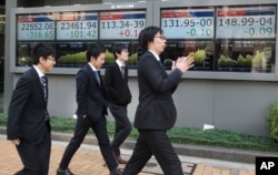 People walk by the electronic stock boards of a securities firm in Tokyo, Nov. 10, 2017. Asian shares sank Friday, following declines on Wall Street after a proposed delay to U.S. tax cut plan dented investor sentiment.