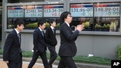 Para pejalan kaki melewati papan elektronik yang menampilkan pergerakan saham di depan sebuah perusahaan sekuritas di Tokyo, 10 November, 2017. Bursa saham Asia melemah akibat rencana pemotongan pajak di Amerika yang tidak menentu. 