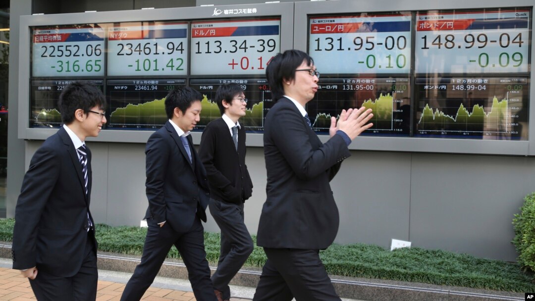 Para pejalan kaki melewati papan elektronik yang menampilkan pergerakan saham di depan sebuah perusahaan sekuritas di Tokyo, 10 November, 2017. Bursa saham Asia melemah akibat rencana pemotongan pajak di Amerika yang tidak menentu. 