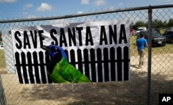 FILE - A man walks past a sign in support of Santa Ana National Wildlife Refuge, home to 400-plus species of birds and several endangered wildcats, at a rally in Mission, Texas, Aug. 12, 2017.