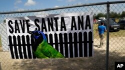 A man walks past a sign in support of Santa Ana National Wildlife Refuge, home to 400-plus species of birds and several endangered wildcats, at a rally in Mission, Texas, Aug. 12, 2017.